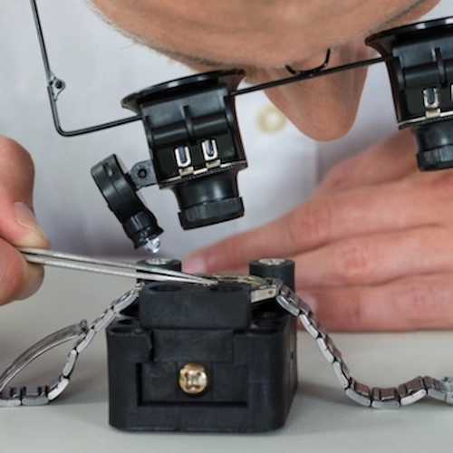 Fotografía de un relojero profesional con lupa (loupe) desmontando cuidadosamente un movimiento mecánico durante un servicio de mantenimiento.